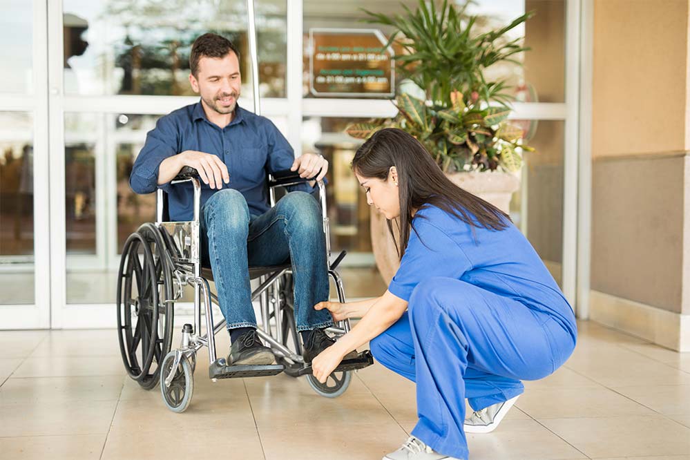Young man in a wheelchair being helps by a nurse